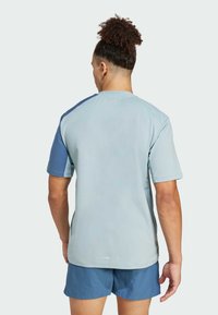 T-shirt sportiva azzurro chiaro con maniche corte e pannelli sulle spalle color blu scuro, caratterizzata da una texture liscia e una scollatura rotonda.