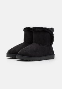 Bottines en cuir suédé noir avec une doublure en fausse fourrure douce, bout arrondi et semelle en caoutchouc texturée. Tige courte avec un détail de revers.