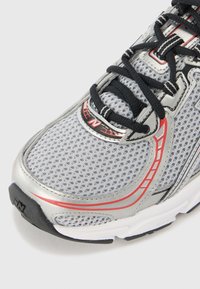 Gros plan d'une chaussure de course grise et argentée avec des lacets noirs, des accents rouges, une tige en mesh respirant et une semelle en caoutchouc blanche.