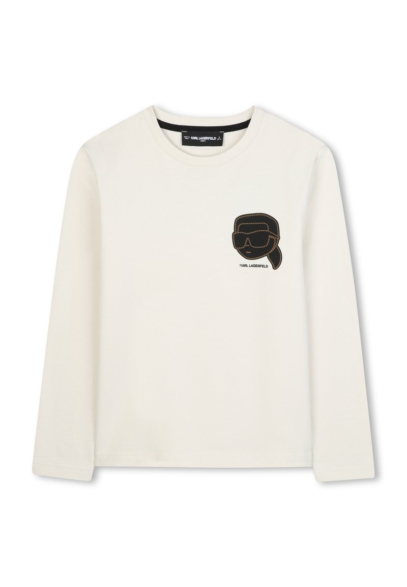 Chemise à manches longues crème avec texture côtelée, présentant un design noir brodé de lunettes de soleil et d'une silhouette de tête sur la poitrine.