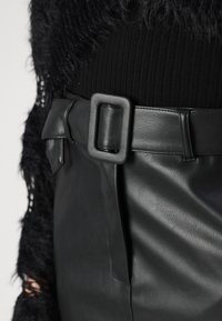 Μαύρη δερμάτινη φούστα με λεία υφή και φαρδύ ζωνάκι με τετράγωνη πόρπη, σε συνδυασμό με μαύρο ριγωτό τοπ με χνουδω�τή επικάλυψη.