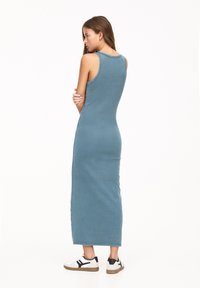 Rochie maxi fără mâneci, ajustată, din material denim albastru cu o textură netedă. Prezintă un decolteu rotund și se termină la nivelul gleznelor.