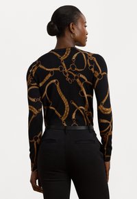 Pulover negru cu imprimeu de lanț aurit, având mâneci lungi și decolteu rotund. Purtați cu pantaloni negri ajustați și o curea subțire neagră.