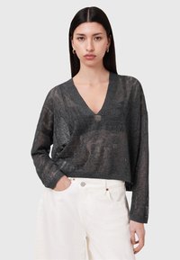 Dunkelgrauer, locker gestrickter Pullover mit V-Ausschnitt und langen Ärmeln, der ein strukturiertes Muster aufweist. Kombiniert mit weißen Hochbundhosen.