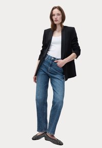 Blazer nero su canotta bianca, abbinato a jeans in denim azzurro chiaro con un motivo testurizzato e ballerine nere a pois.