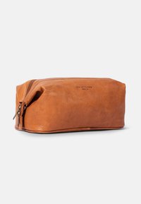 Tan leather toiletry bag with a rectangular shape, zip closure, and embossed brand name. Smooth texture and minimalistic design.
