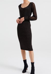 Schwarzes Midikleid mit Rundhalsausschnitt, tailliertem Oberteil und plissierten, transparenten Ärmeln, aus einem strukturierten, schimmernden Stoff gefertigt. Akzentuiert durch kniehohe Stiefel.