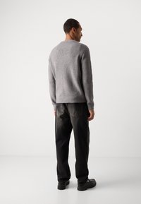 Gray ribbed knit sweater with a round neck, paired with dark trousers and black shoes. The design features a textured finish and relaxed fit.
