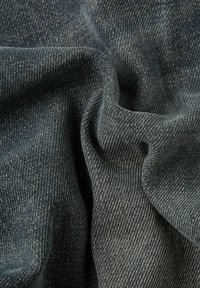 Donkerdenim stof met een subtiele textuur, die een klassieke twillbinding toont en een gekreukt uiterlijk heeft, wat de zachtheid en flexibiliteit benadrukt.