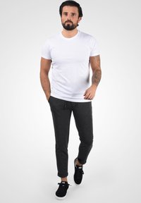 Camiseta blanca de manga corta combinada con pantalones jogger entallados en gris oscuro y zapatillas negras, con cintura elástica y tejido suave.