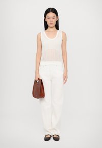 Baltas adīts topiņš ar ovālu kakla izgriezumu, apvienots ar augsta vidukļa baltām džinsu biksēm. Tur rokās brūnu ādas rokassomu, uz kājām plakanas kurpes.