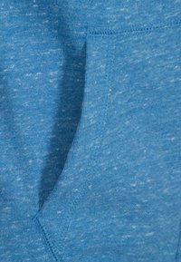 Tela de sudadera azul claro con una superficie suave y texturizada; cuenta con un bolsillo frontal y costuras reforzadas en los bordes.