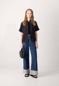 Svart linneskjorta med kort ärm, åtsittande svart linne, högmidjade blå jeans med vida ben och fransade grå manschetter, texturerad svart handväska och svarta sandaler.