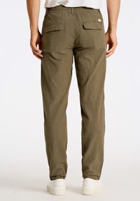 Pantalones verdes oliva ligeros con cintura elástica, bolsillos traseros y piernas ajustadas. Hechos de una tela texturizada, combinados con zapatillas blancas.