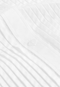 Tissu blanc plissé avec une texture lisse, présentant un détail de bouton transparent. Les plis sont espacés de manière uniforme pour un aspect structuré.