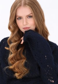 Granatowy sweter wykonany z dzianiny o teksturowanym wykończeniu oraz otwartym splocie na mankietach, w połączeniu z luźnymi, falującymi włosami.