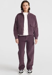 Purple cord jacket with high collar and two front pockets, paired with matching cargo pants featuring side pockets, and black and white sneakers.