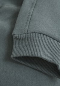 Grå tröja med mudd som har en texturerad ribbad stickning och slät bomull, med en platt sömdetalj längs kanten.