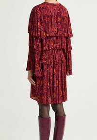 Robe à volants superposés avec un motif rouge et orange, manches longues et col haut, associée à des bottes violettes brillantes montantes jusqu'aux genoux.