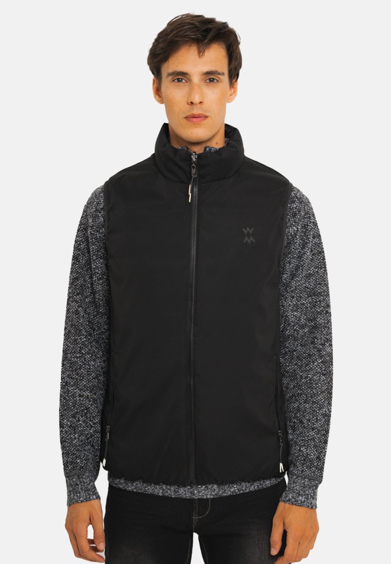 Veste noire sans manches avec col montant et fermeture éclair intégrale. Confectionnée en tissu lisse, avec des poches latérales et un détail de logo subtil sur la poitrine.