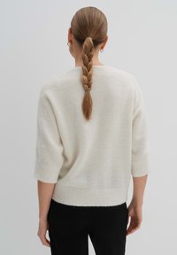 Elfenbeinfarbener, weicher Strickpullover mit verkürzten Ärmeln und geripptem Saum, der eine lockere Passform und glatte Textur zeigt. Die Rückansicht zeigt ein einfaches Design.