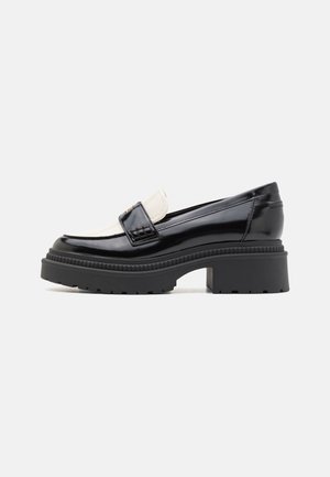 Black patent leather loafers with a white leather panel, chunky black rubber sole, and slight heel. Textured stitching detail on the upper.
