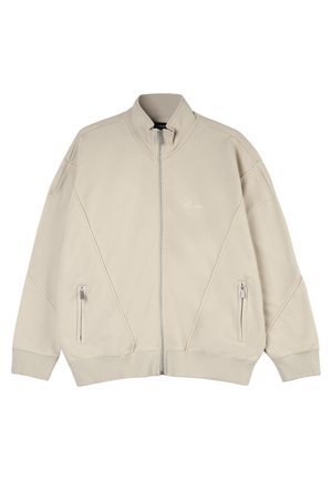 Beige zip-up jacket with high collar, featuring two side pockets, textured fabric, and diagonal stitch design on the front.