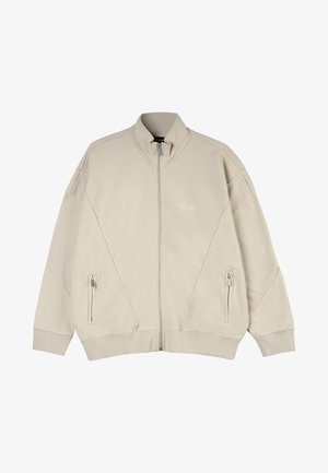 Beige zip-jakke med høj krave, der har to sidelommer, tekstureret stof og skrå syning på fronten.