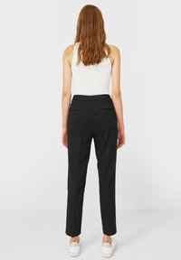 Zwarte gepinstripe broek met een getailleerde pasvorm, voorzien van zijzakken en een tailleband. Gemaakt van een gladde stof, gecombineerd met witte sneakers.