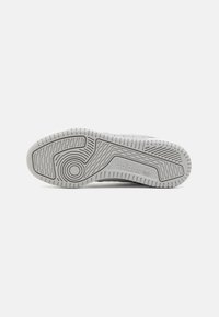 Suela de zapato de goma gris claro con patrones texturizados, que incluyen surcos circulares y lineales, y logo de la marca embosado.