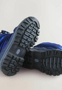 Blaue Wanderschuhe mit strukturierten Gummisohlen, die über tiefe Profilierungen für bessere Bodenhaftung sowie graue Akzente an den Seiten und der Ferse verfügen.