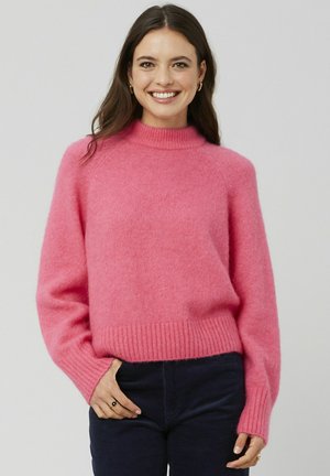 Pull en tricot rose avec un col montant, une bordure côtelée et des manches longues. Texture douce, coupe décontractée et sans motifs ni accents visibles.