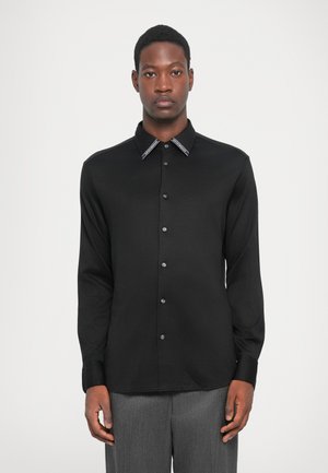 Black long-sleeve shirt with a subtle sheen, featuring a pointed collar with contrasting trim and button closure, made from smooth material.