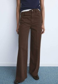 Bruine pantalon met wijde pijpen van katoen, met een hoge taille, voorzakken en een vervaagde textuur. Draagt een marineblauwe top.