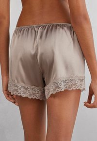 Satinshorts i taupe med spetsdetaljer vid fållen. Har ett elastiskt midjeband och en slät, glansig yta.