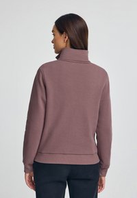Sudadera de forro polar con cuello alto, en un tono malva suave, que presenta un corte holgado y puños acanalados. Textura lisa con un diseño sencillo.
