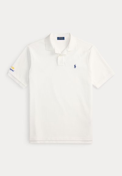 Λευκό πόλο με κοντό μανίκι και μπλε λογότυπο Polo Ralph Lauren στο στήθος και λογότυπο "US Open" στο αριστερό μανίκι, τοποθετημένο επίπεδα σε λευκό φόντο.