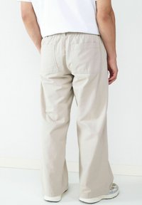 Persoon in losse beige broek met elastische tailleband en opgestikte zakken, gecombineerd met witte sneakers en een wit shirt.