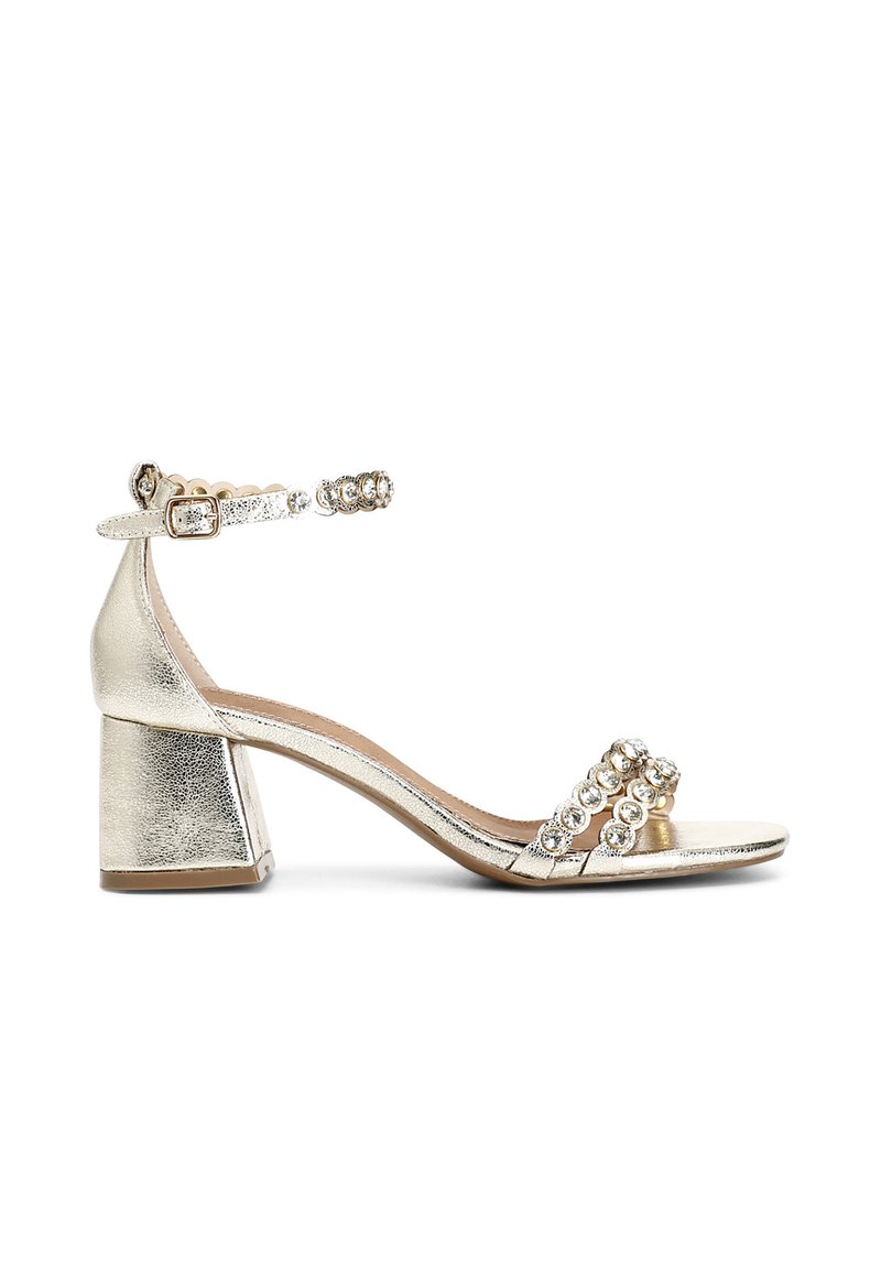 Kulta metalliset korkokengät, joissa on lohkokorko, koristeellinen nilkkahihna pyöreillä jalokivikoristeilla ja kaksi etuhihnaa.