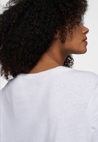 T-shirt bianco in cotone con vestibilità rilassata, caratterizzato da un colletto rotondo e tre dettagli di cuciture orizzontali sul retro vicino al collo.