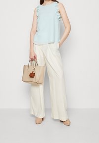 Top senza maniche blu chiaro con spalline a ruches, abbinato a pantaloni larghi bianchi a righe e borsa beige con un accento marrone.