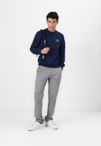 Sudadera navy con un pequeño logo en el pecho, pantalones grises de corte relajado y zapatillas blancas, con una tela texturizada y un diseño sencillo.