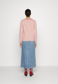 Gestreiftes Langarmhemd in Rosa und Weiß, kombiniert mit einem blauen Jeans-Maxirock. Rote Stiefel mit dekorativen weißen Akzenten.