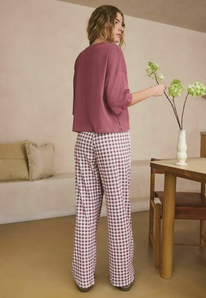 Tmavohnedý krátky rukáv s voľným strihom a bočnými rozparkami v kombinácii so širokými bielymi nohavicami s bordovým kockovaným vzorom.