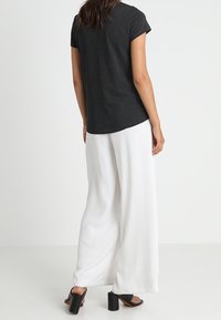 Svart kortärmad topp med rundad nederkant, kombinerad med vita vida byxor. Outfiten har en mjuk textur och klacksandaler med blockklack.