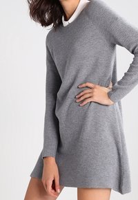 Abito maglione grigio a coste con maniche lunghe e colletto bianco. Presenta una vestibilità rilassata e un orlo leggermente svasato per favorire il movimento.
