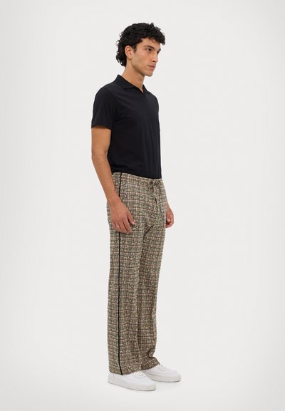 Black short-sleeve polo shirt paired with plaid wide-leg trousers featuring a multi-color pattern and black side stripes. White sneakers complete the look.