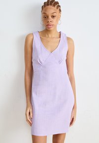 Lila mekko ilman hihoja, V-pääntie, hienoinen löystyminen, teksturoitu kangas ja kerrostuma rintakehän alla. Minimalistinen muotoilu.