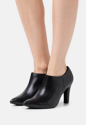 Bottines noires à talons hauts avec une finition texturée en motif crocodile et un design à bout pointu. Extérieur lisse et forme effilée.