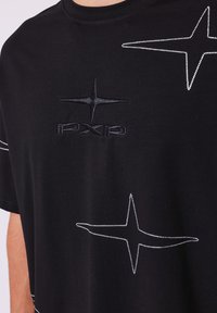 Zwarte katoenen T-shirt met een textuur van het zwarte logo "PXP" en witte stergraphics omlijnd met witte stiksels. Korte mouwen, ontspannen pasvorm.